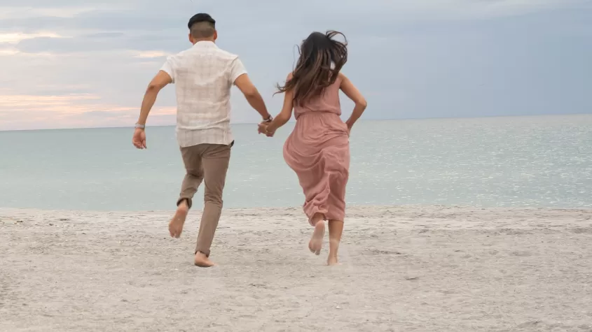 Couple running towards the ocean holding hands