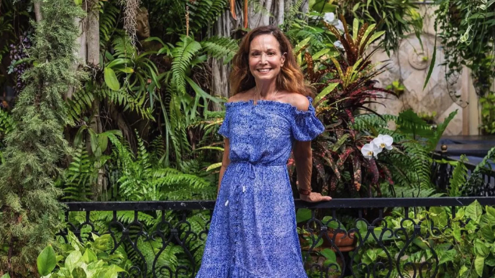 A woman poses in front of a lush botanical garden